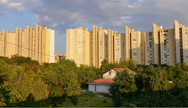U prvom planu je zelenilo u kome je mala kućica. Iza parkića uzdižu se brojni visoki neboderi koji isto izgledaju(iste su visine i boje).