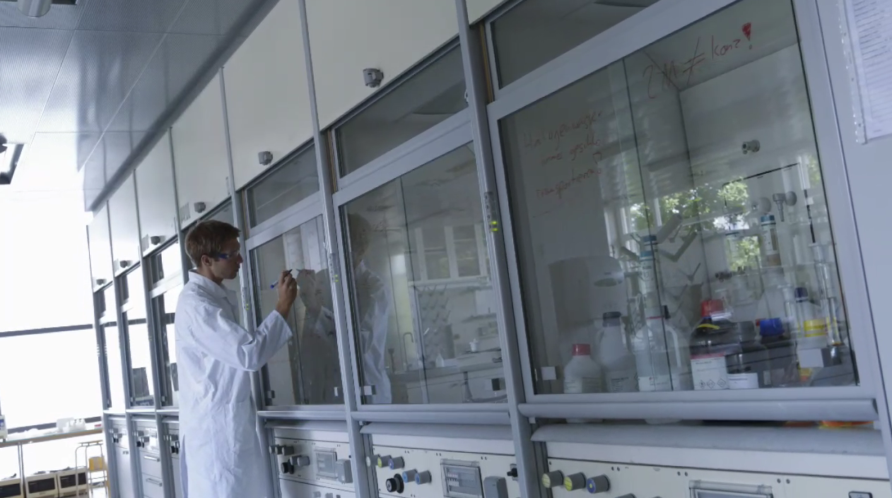 Fotografija prikazuje digestor ispred kojeg stoji mladi znanstvenik