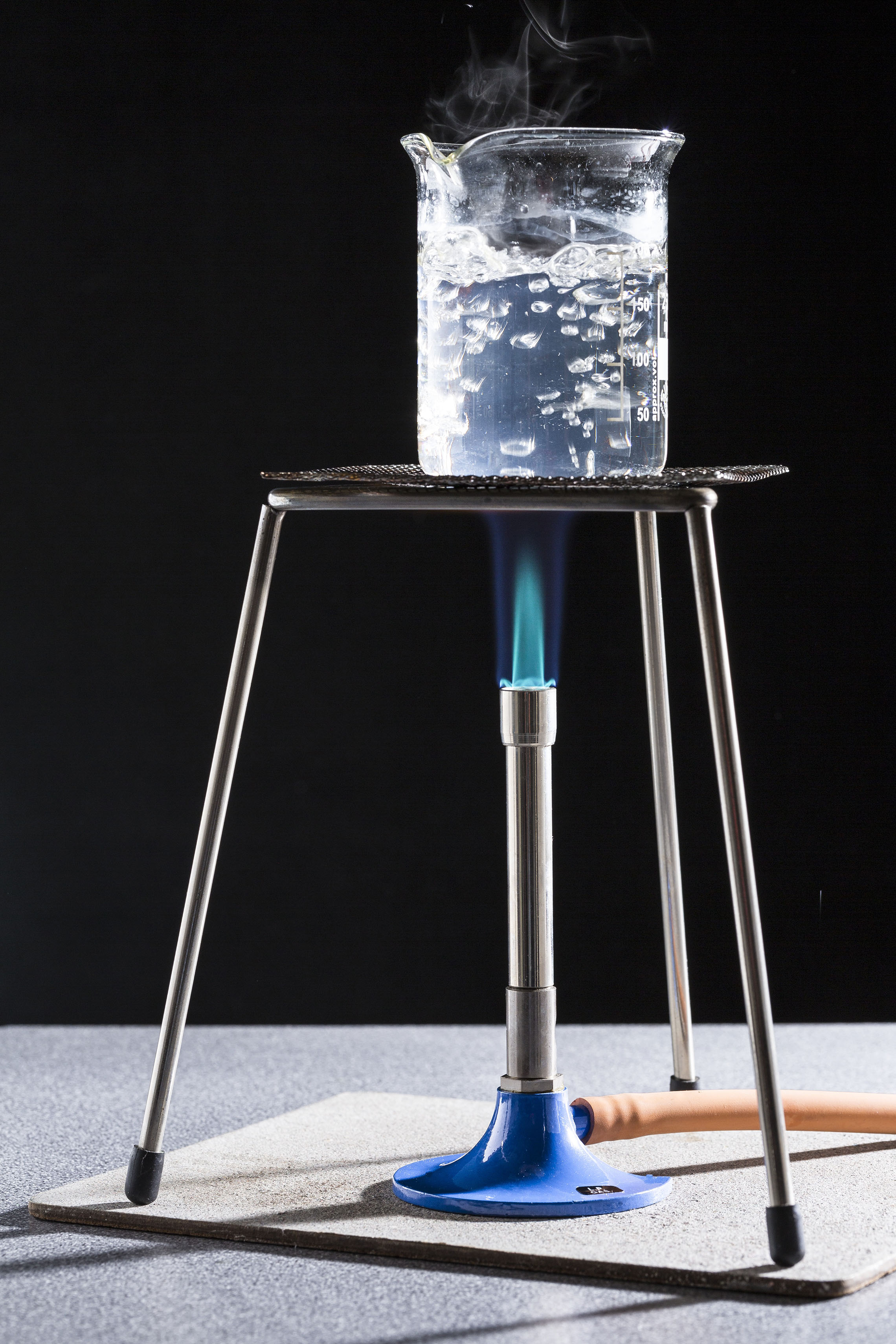 Fotografija prikazuje d.estiliranje vode koja vrije vrije pri temperaturi od 100 °C pri standardnom atmosferskom tlaku. Vidi se plamenik iznad kojeg je postavljena staklena posuda s vodom.