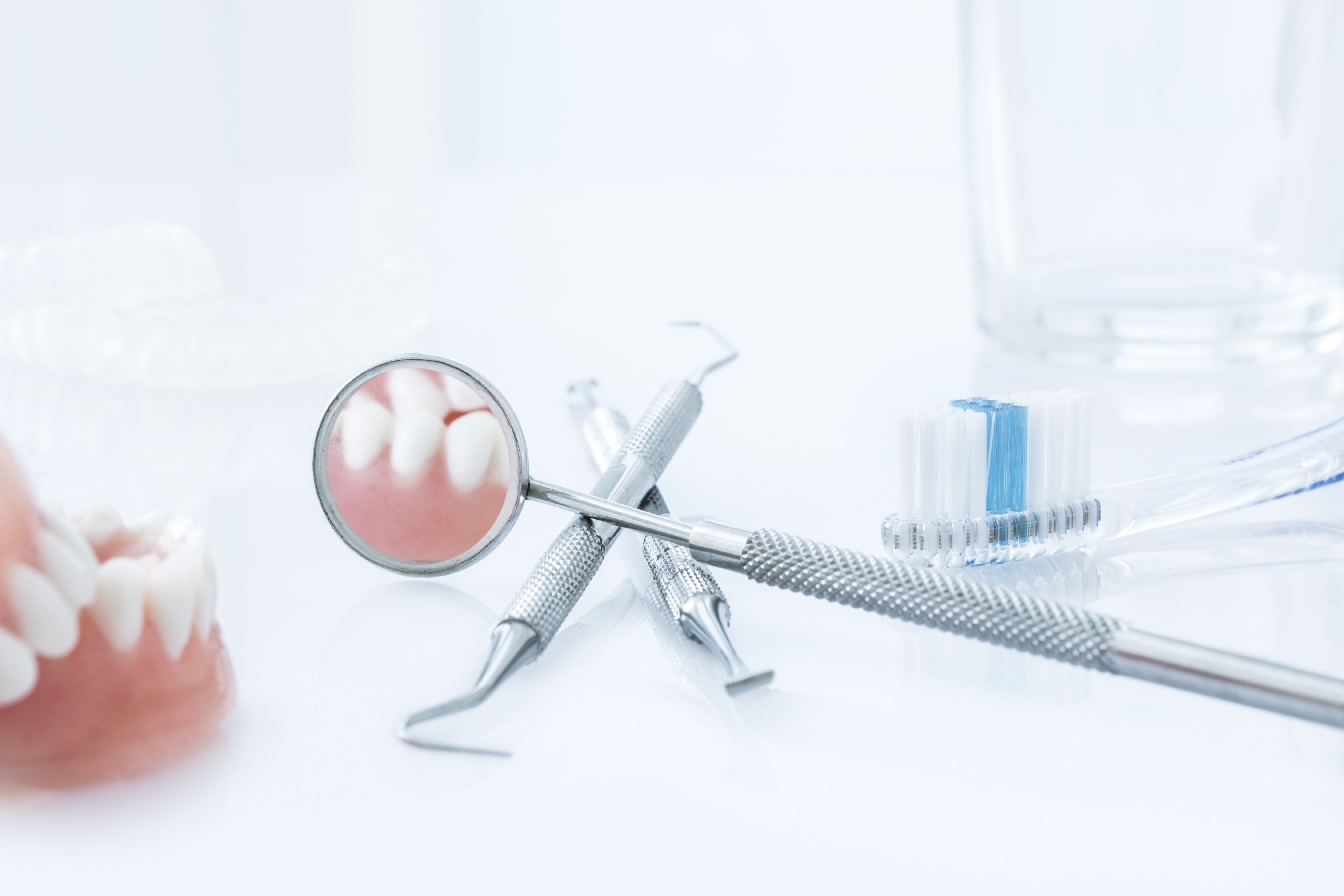 Prikazan je model zubiju, pribor doktora dentalne medicine (ogledalce, kompozit) te četkica za zube.