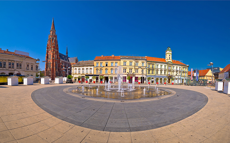 panoramska snimka trga s kružnim podnim vodoskokom. Na lijevoj strani trga je katedrala crvene boje(izgrađena fasadnom ciglom), zatim nekoliko lijepo uređenih žutih zgrada. Na trgu su i male drvene mobilne kućice 