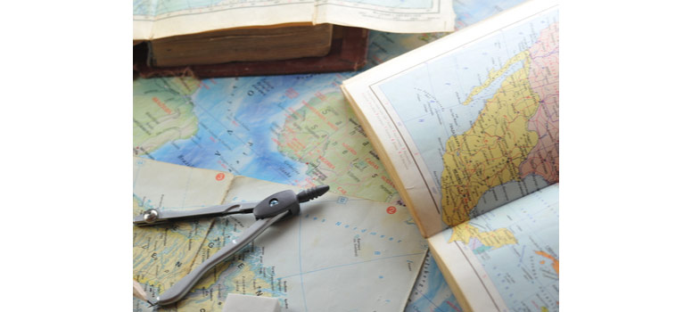 Na fotografiji se nalazi karta svijeta, otvoreni atlas, otvorena knjiga te šestar