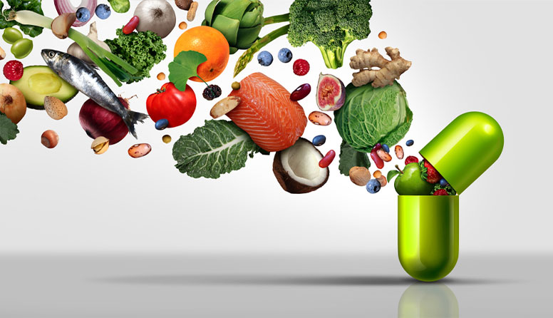 Fotografija prikazujevoće, povrće, ribu, orašide, grahorice kako izviru iz kapsule koja predstavlja tabletu vitamina.