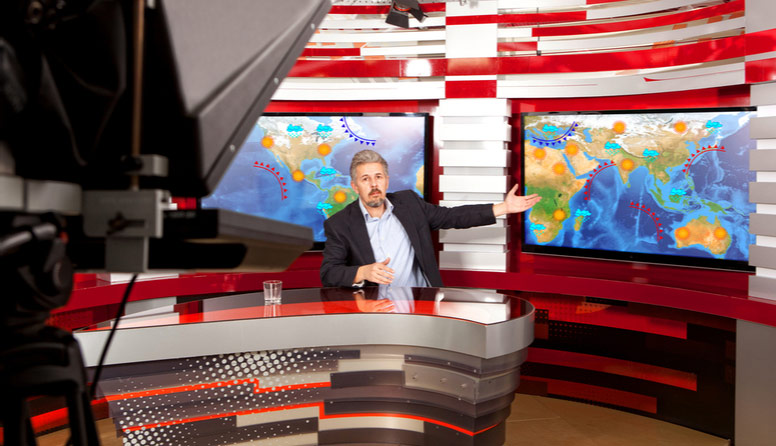 Čovjek koji sjedi u televizijskom studiju i rukom pokazuje na sinoptičku kartu na ekranu