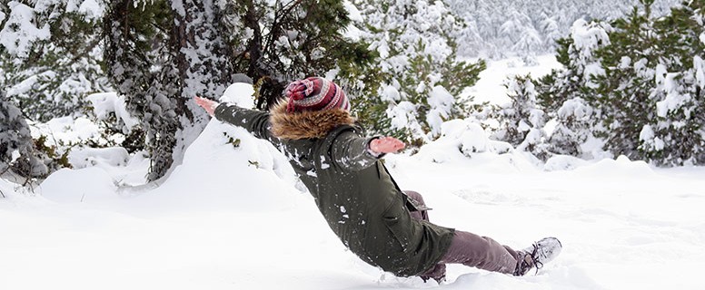 Dijete leđno pada raširenih ruku na rahlu snježnu površinu. U pozadini je snjegović i snježni pejzaž borove šume.