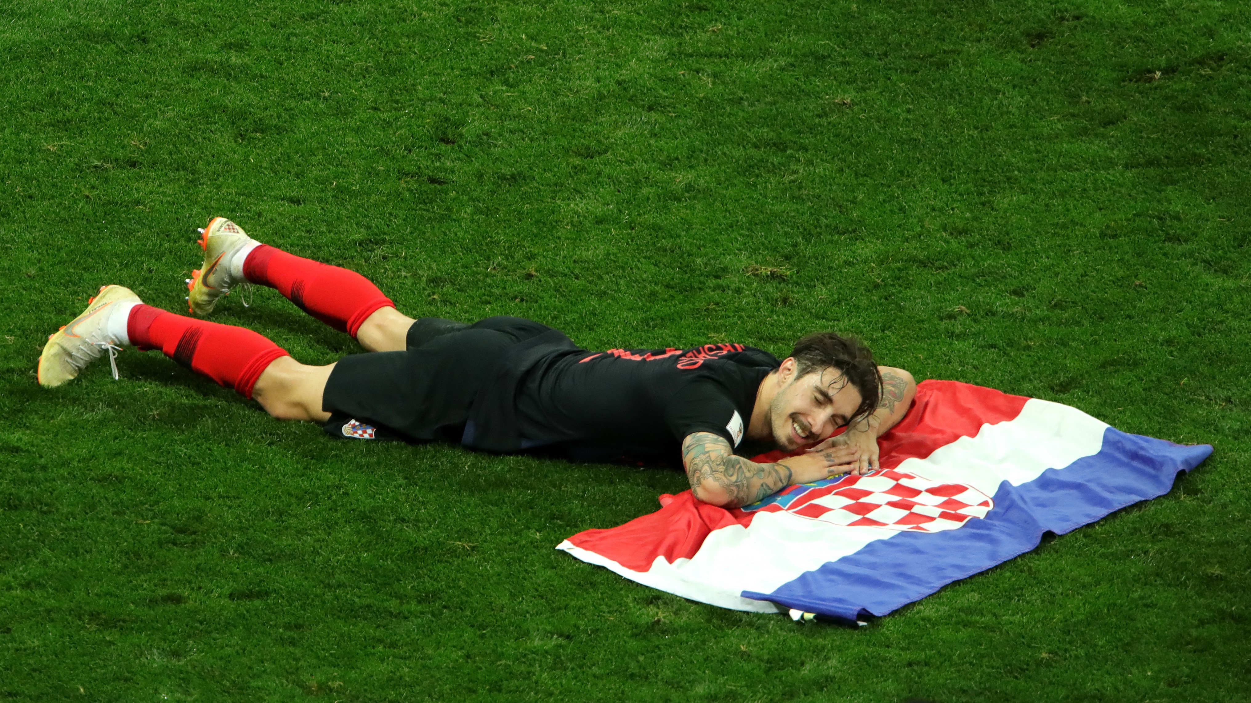 Šime Vrsaljko, naš desni bek, leži na nogometnom travnjaku radosnog izraza lica dok mu ruke i glava počivaju na položenoj hrvatskoj zastavi.