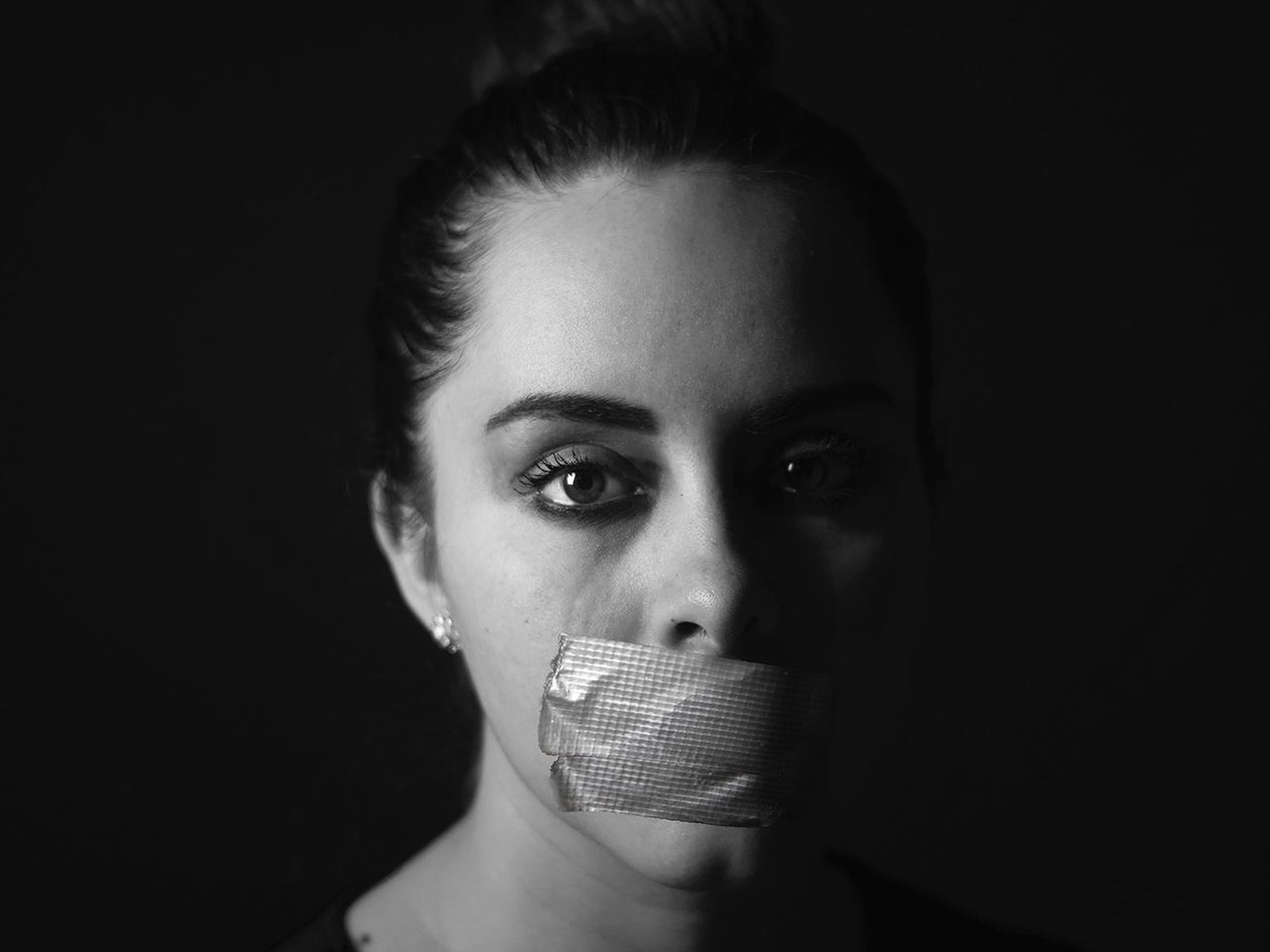 Crno-bijela fotografija žene koja preko usta ima ljepljivu traku, selotejp. 