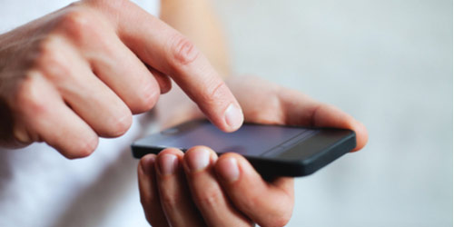 Prikazani dlanovi osobe. Lijevi dlan drži smart phone. Kažiprstom druge ruke dodiruje ekran mobitela.