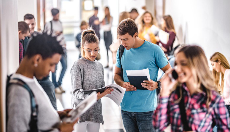 Djevojka i mladić razgovaraju u školskom hodniku. U ruci drže bilježnice. Djevojka pokazuje sadržaj u otvorenoj bilježnici.