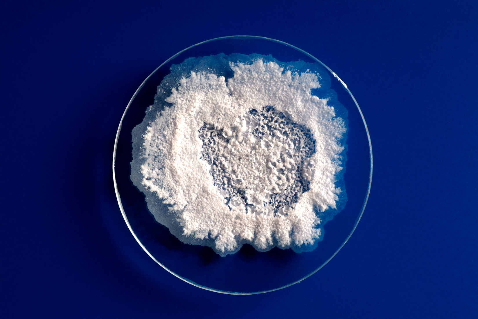 Na slici je prikazano satno stakalce okruglog oblika na kojem se vidi bijela mrlja soli. Stakalce je na tamnoplavoj podlozi.