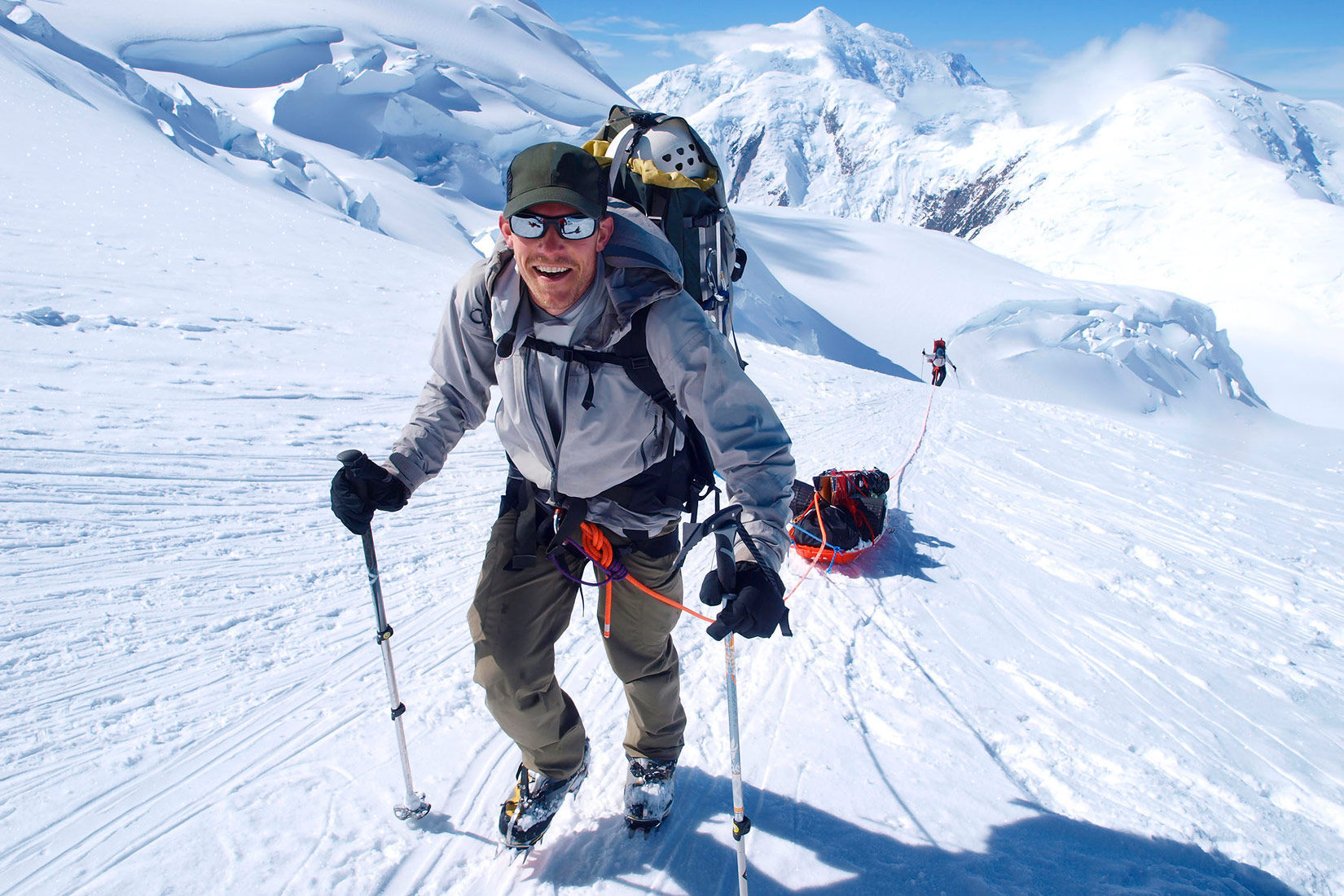 Na fotografiji je prikazan alpinist. Nasmiješen gleda u fotografa. Na leđima ima naprtnjaču, a u rukama štapove.Ima naočale za skijanje. Za sobom vuče sanjke s opremom. Uže kojim ih vuče zavezano mu je oko struka.