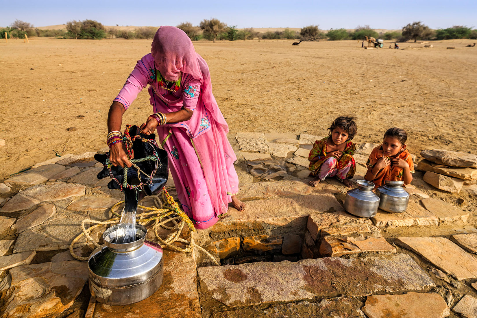 Na zemlji je prikazana žena kako iz bunara, koji izgleda poput rupe u zemlji, vadi vodu. Nedaleko od nje čuči dvoje male djece. Okruženi su pustinjskim okolišem siromašne vegetacije. U zemljama trećeg svijeta je veliki nedostatak vode.
