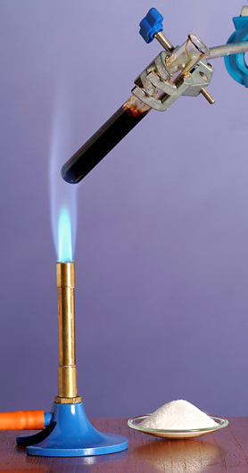 Fotografija prikazuje zagrijavanje šećera saharoze. Saharoza, koja je inače bijele boje, stavljena je u epruvetu. Epruveta je stavljena iznad plamenika. Saharoza se zagrijala i pocrnjela.