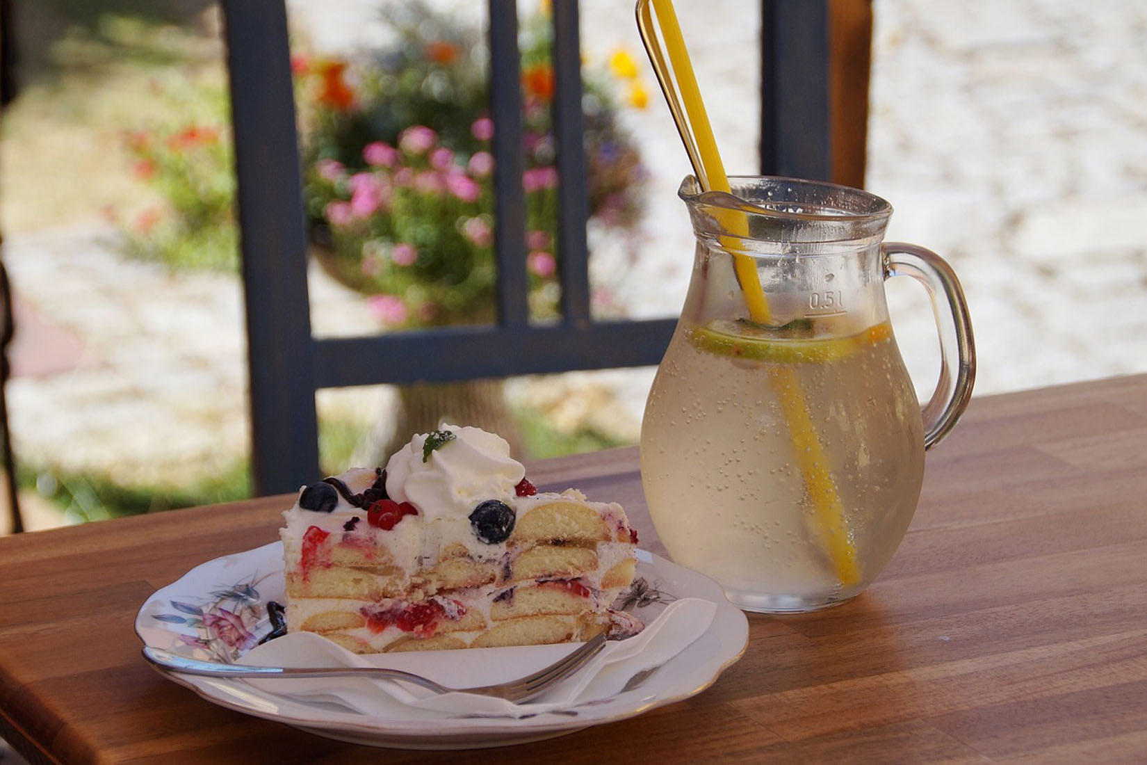 Fotografija prikazuje komad torte od višanja sa šlagom i vrč s limunadom.