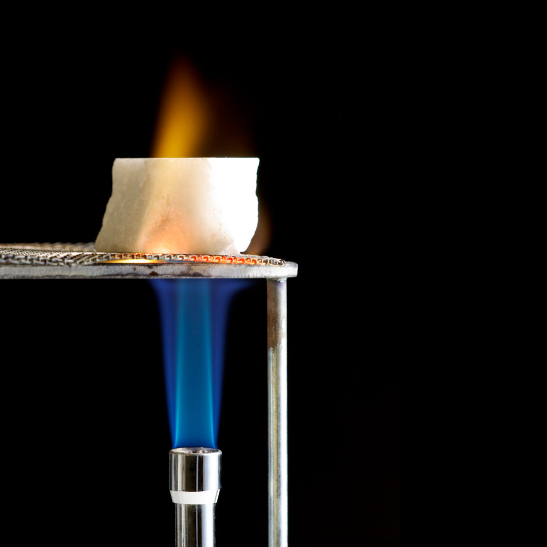 Fotografija prikazuje žarenje komadića mramora na mrežici iznad plamenika.