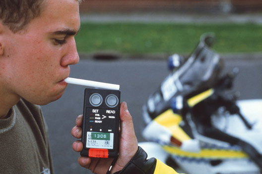 Fotografija prikazuje mjerenje volumnog udjela alkohola u dahu vozača pomoću aparata koji se sastoji od četvrtaskog kućišta veličine mobitelja i cjevčice u koju vozač upuhuje dah.