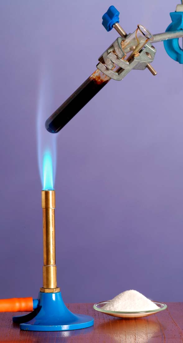 Slika prikazuje zagrijavanje šećera u epruveti iznad plamenika.Plamenik ima plavo postolje a gornji dio je bakrene boje. Dijelom se vidi narančasta cijev na dnu plamenika koja dovodi plin.Epruveta je u gornjem dijelu pričvršćena držačem za epruvete koji izgleda kao hvataljka s vijkom . Pokraj plamenika je okrugla zdjelica sa sitnim bijelim šećerom. Epruveta je u kosom položaju iznad plameniku. Šećer u epruveti je crne boje i nastala je nova tvar. Znači da je došlo do kemijske promjene.