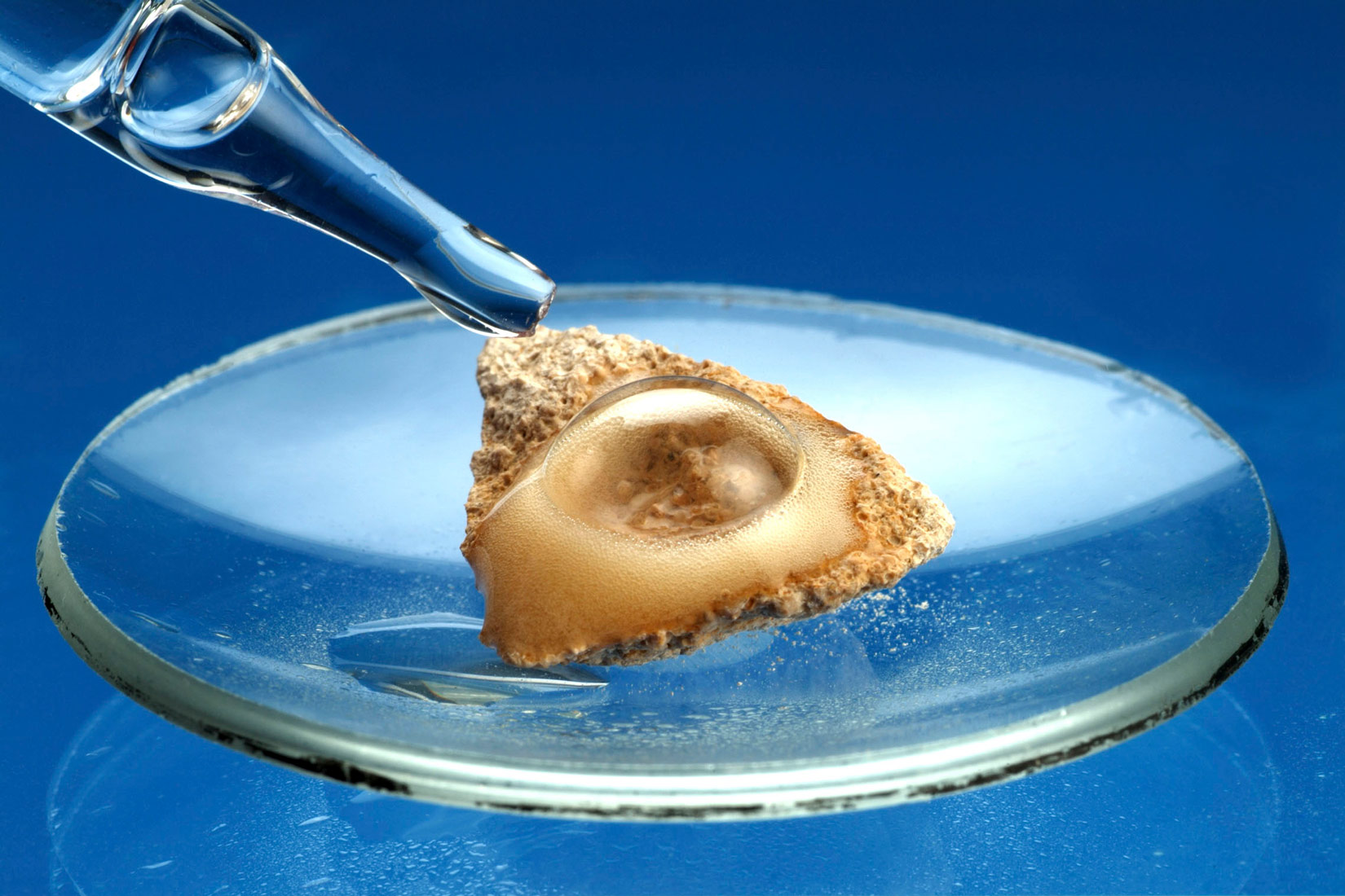 Fotografija prikazuje reakciju kiseline i kamenca. Nakon što se na kamenac nakapa kiselina, na površini kamenca pojavljuju se mjehurići.