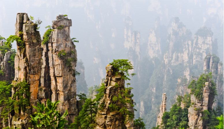 Tropski krš, Kina. Fotografija prikazuje kamene strukture koje nalikuju na stupove izgrađene od naslaganog kamenja. Strukture su djelomično pokrivene zelenim biljem i uzdižu se iznad velikog ponora