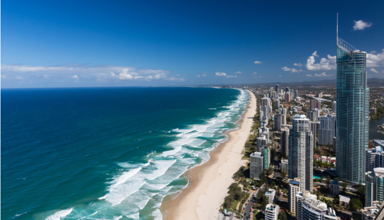 Zlatna obala, Australija. Fotografija prikazuje kilometrima dugačku usku pješčanu plažu koju oplakuju oceanski valovi. Plaža se smjestila između modrog oceana i niza visokih modernih nebodera