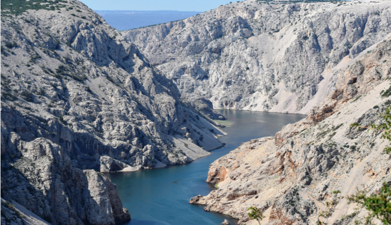 Kanjon Zrmanje. Fotografija prikazuje vijugavu plavu rijeku koja teče kroz stjenoviti, goli krški krajolik kojim dominiraju nijanse sive boje
