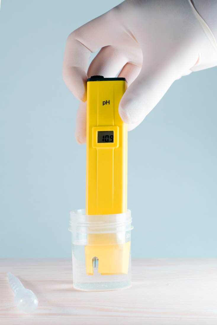 Fotografija prikazuje ruku koja u prozirnu posudu uranja uređaj žute boje pod nazivom pH-metar. To je instrument koji se koristi za mjerenje pH-vrijednosti najčešće tekućih uzoraka.