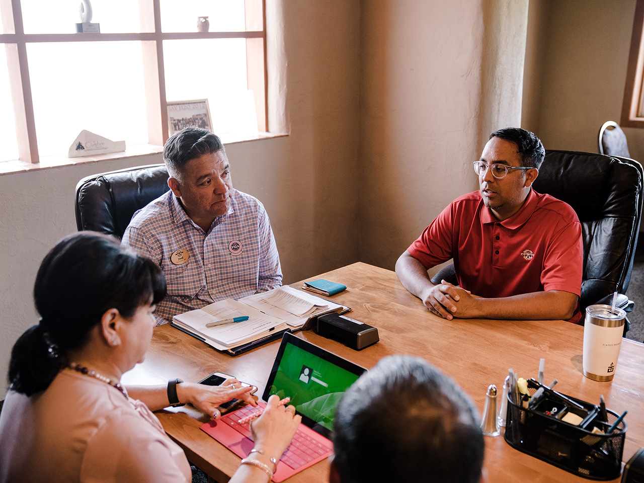 Tamnoputi muškarac s naočalama i u bordo polo majici sjedi za stolom i govori dok ga tri člana komisije ozbiljno promatraju. 