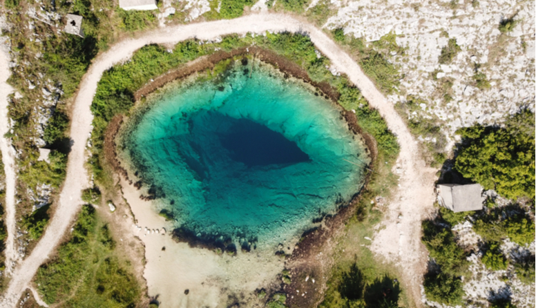Izvor Cetine. Slika prikazuje jezero nalik na plavo oko sa modrom zjenicom u krškom krajoliku
