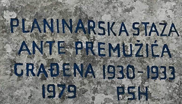 Premužićeva staza. Fotografija prikazuje stijenu na kojoj je plavom bojom napisano: Planinarska staza Ante Premužića građena 1930 - 1933, 1979 PSH. 