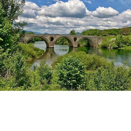 Kameni most sa tri luka koji prelazi preko zeleno plave rijeke. Most se ogleda, zrcali u voi. Oko rijeke i mosta je zelenilo,Na dva središnja stupa mosta su dvije okrugle rupe-otvori.