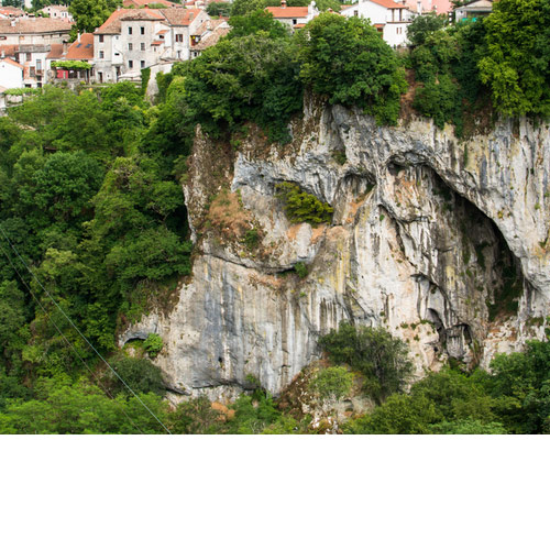 pazinska jama. Sivo smeđa stijena, na vrhu se vidi naselje, a cijela stijena je po rubovima okružena zelenilom.