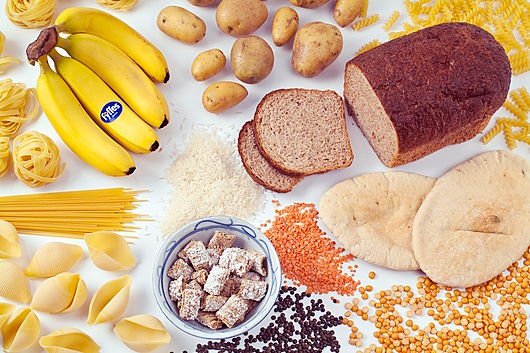 Slika prikazuje namirnice bogate ugljikohidratima: tjesteninu, kruh, krumpir, rižu, žitarice, banane i mahunarke.
