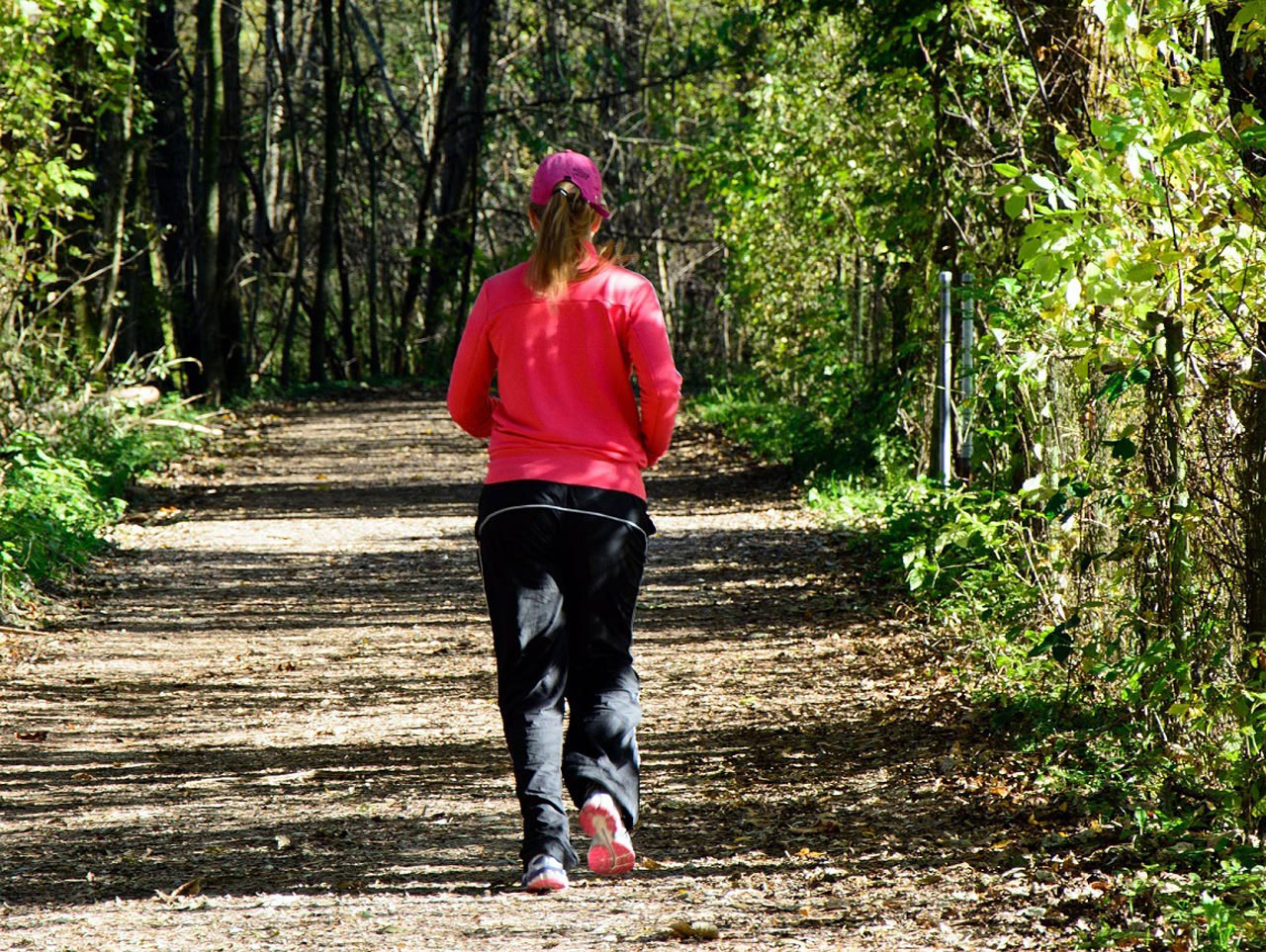 Fotografija prikazuje ženu koja trči stazom u prirodi.