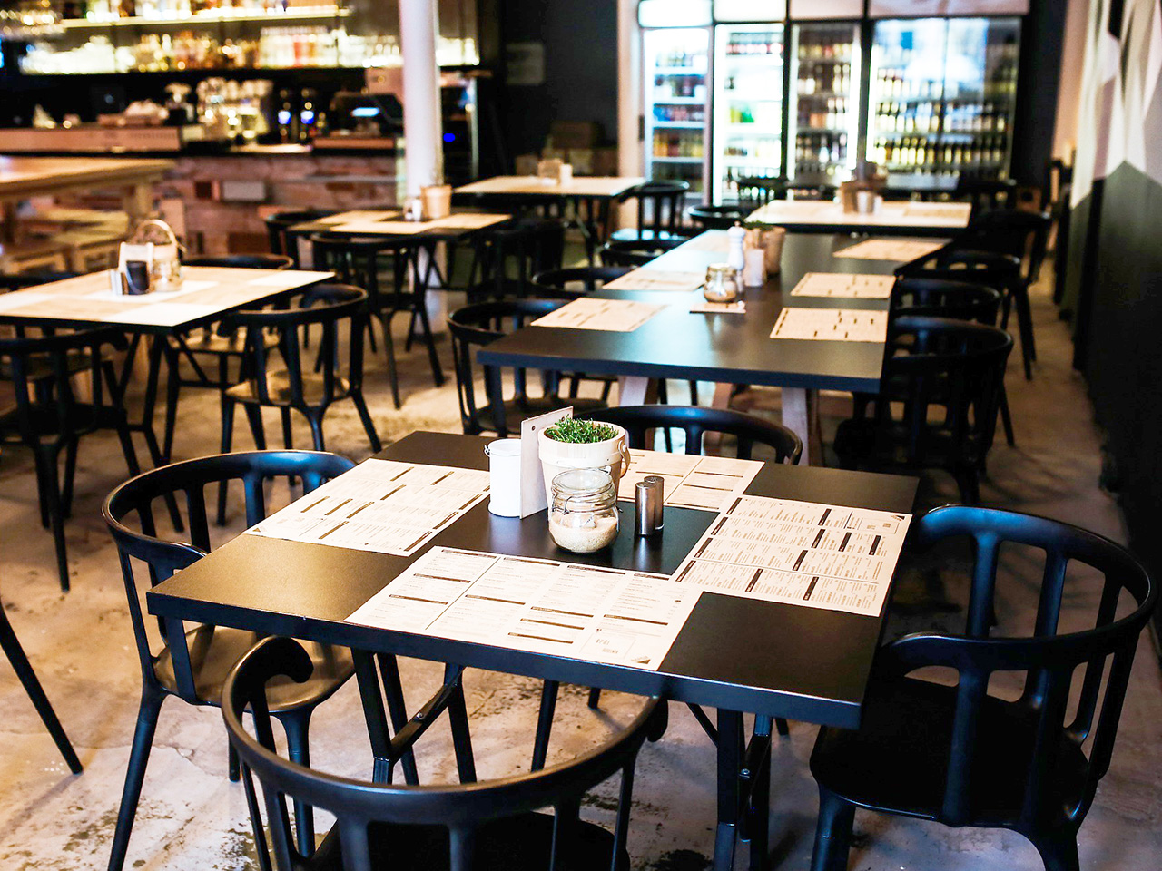 Restoran s crnim stolovima i stolicama. Na stolovima se nalaze jelovnici koji ujedno služe kao podmetači. 
