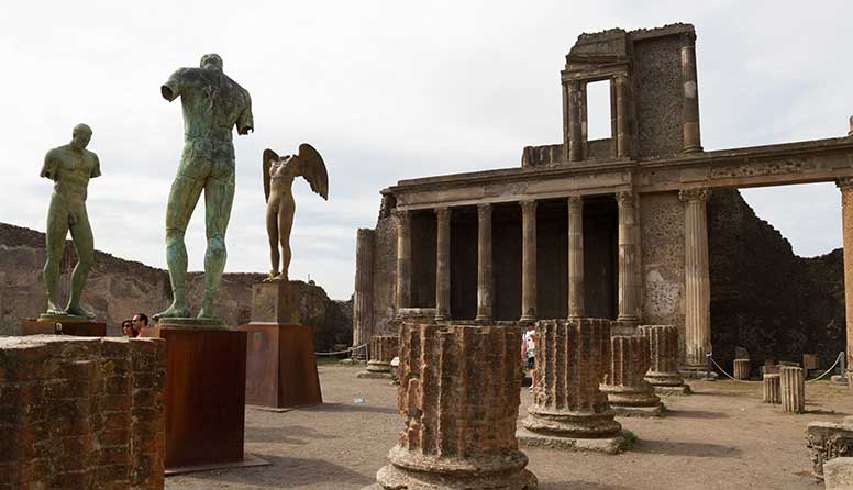 Na fotografiji se vide tri skulpture izložene na forumu. U pozadini su ostatci hrama.